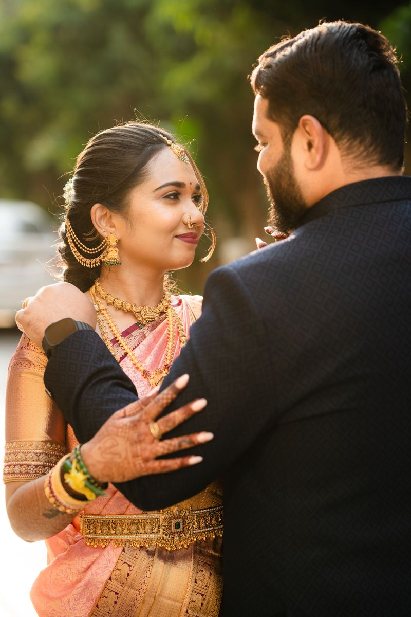 An elegant couple in traditional Indian attire embracing outdoors during a sunset wedding ceremony.