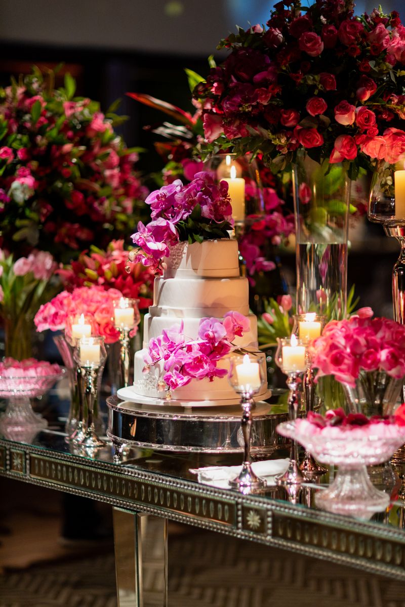 A beautifully decorated wedding cake surrounded by vibrant floral arrangements and candles creating a romantic ambiance.