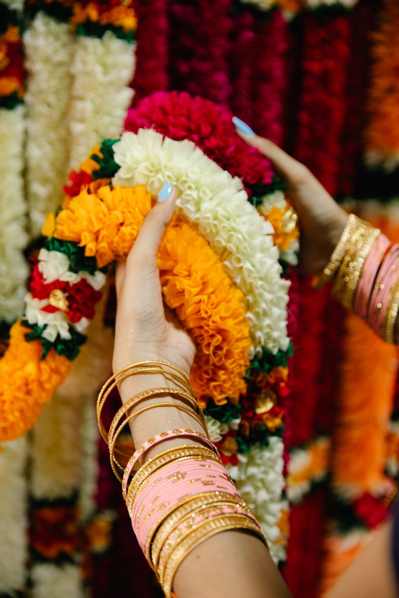 Woman's hands holding vibrant flower garlands, adorned with gold bracelets.